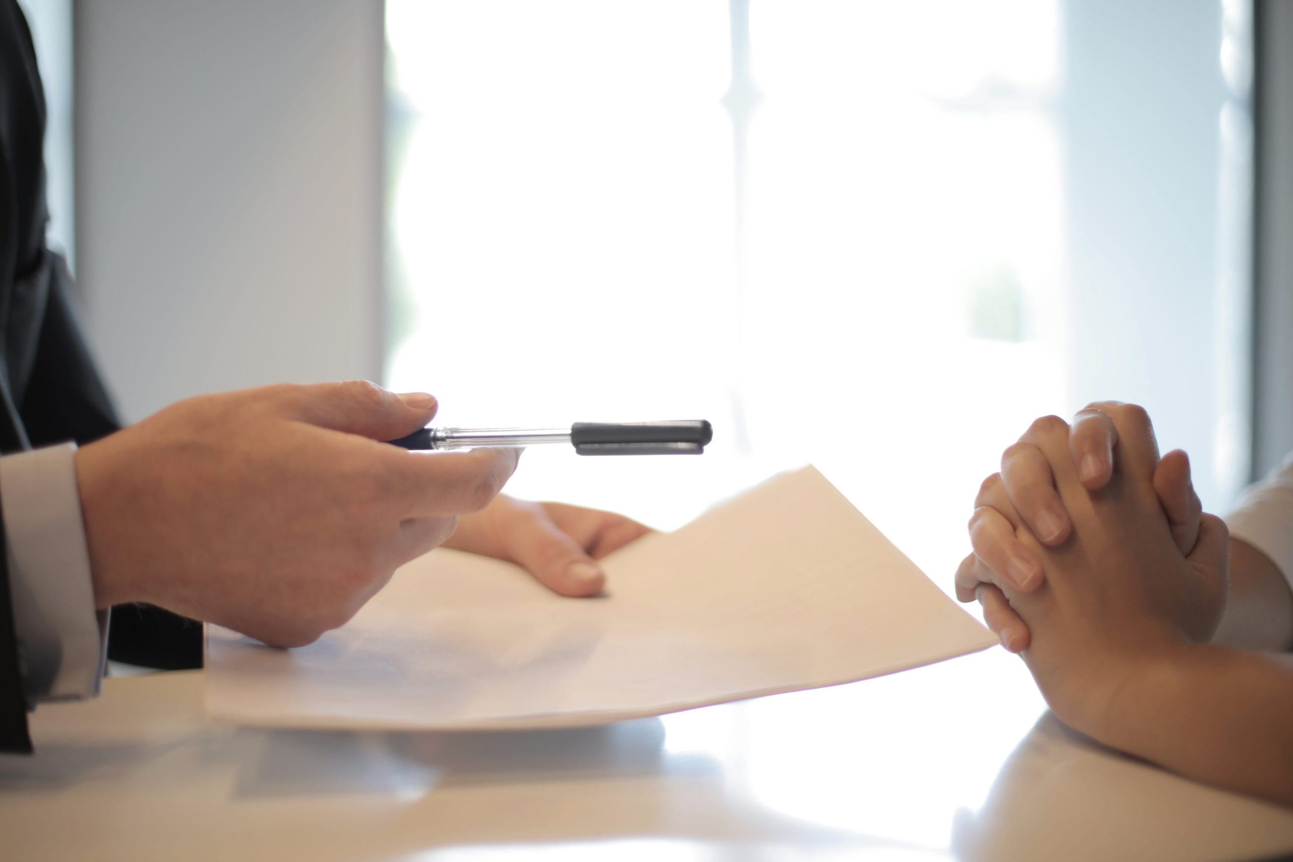 Close up of male property manager's hands offering a pen and contract to a female's hands.