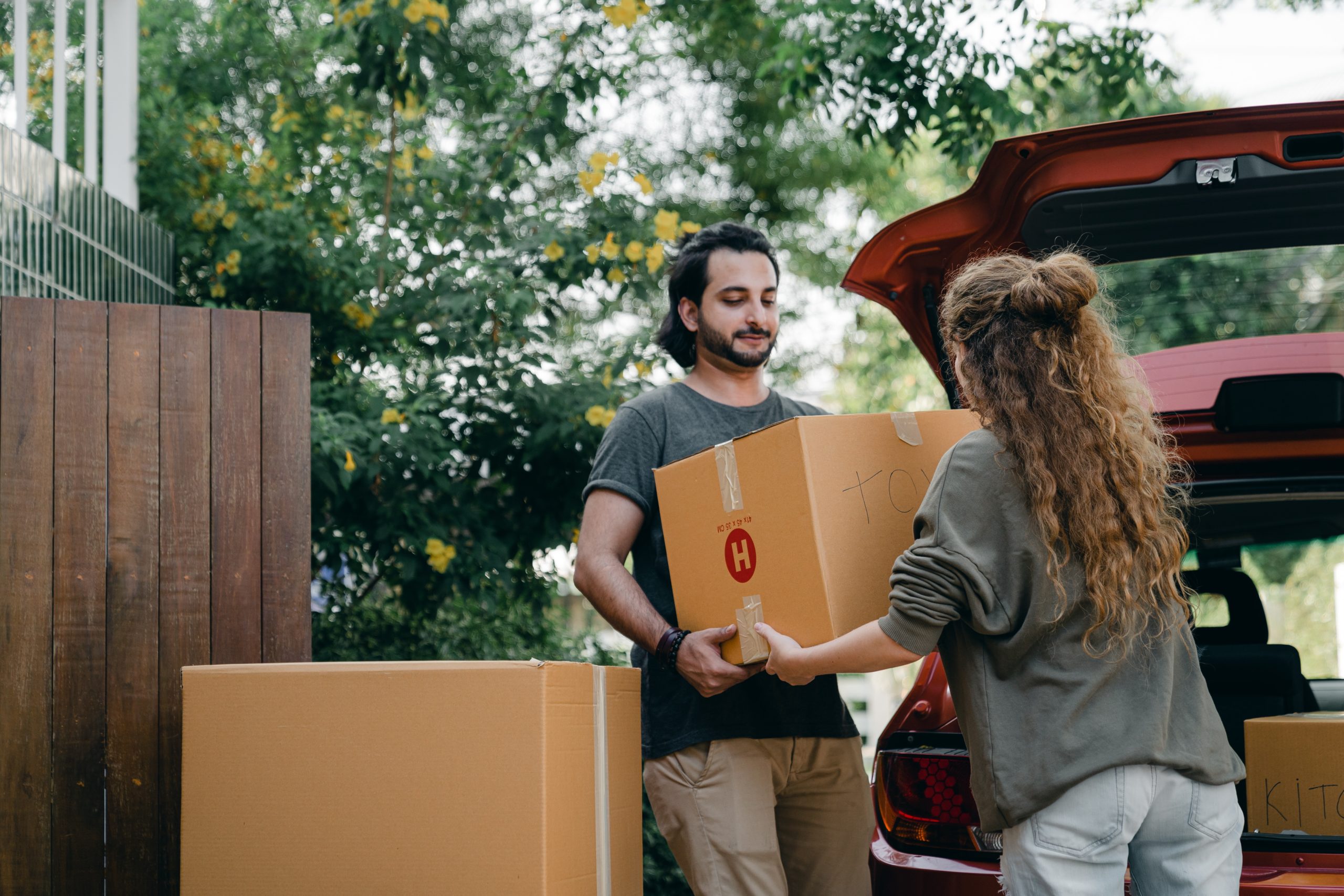 Man and woman millenial couple unloading moving boxes from a car.