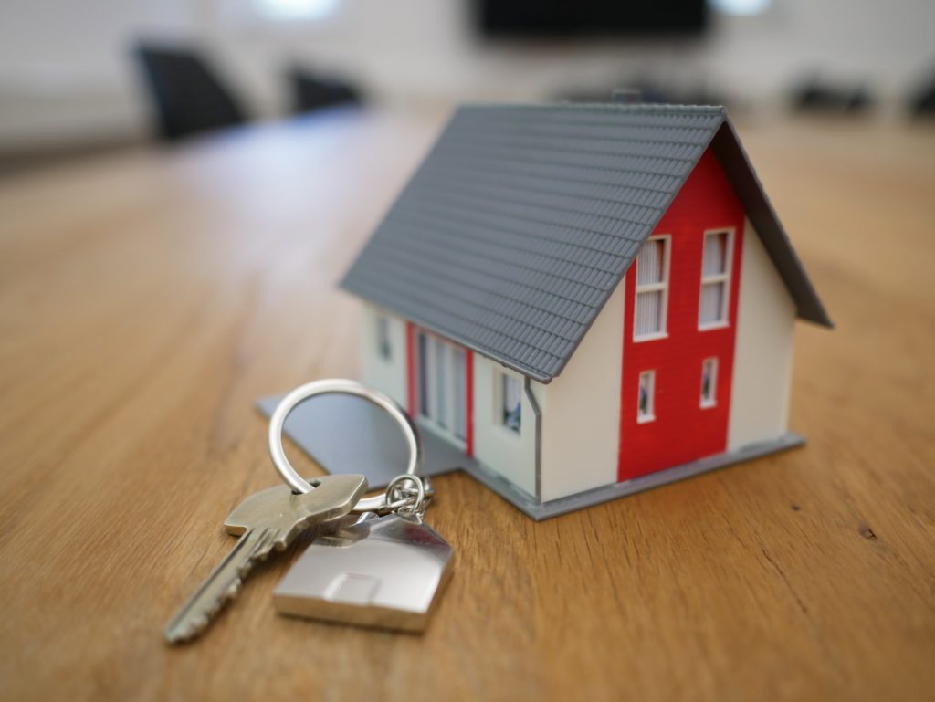 Small replica house on wooden office table next to house keys.