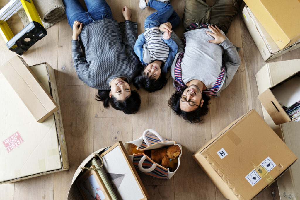 Asian family laying on floor in their new home in Durham, NC, surrounded by moving boxes.