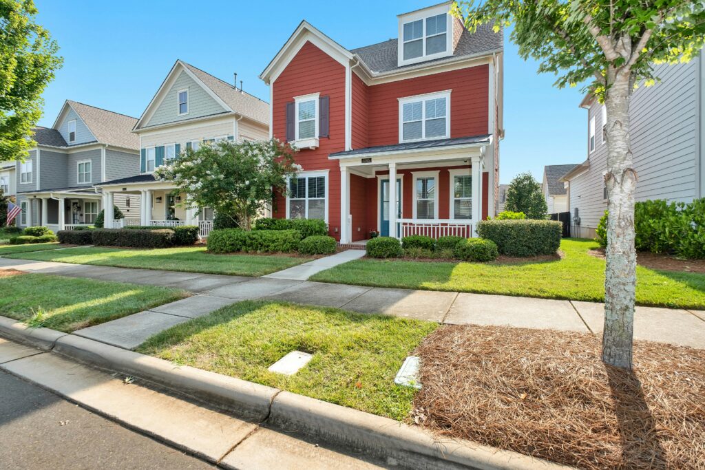 Row of houses in a neighborhood, with adorable two-story red house with small front porch in foreground. .